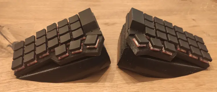 Two assembled black low-profile Corney halves on a wooden desk.